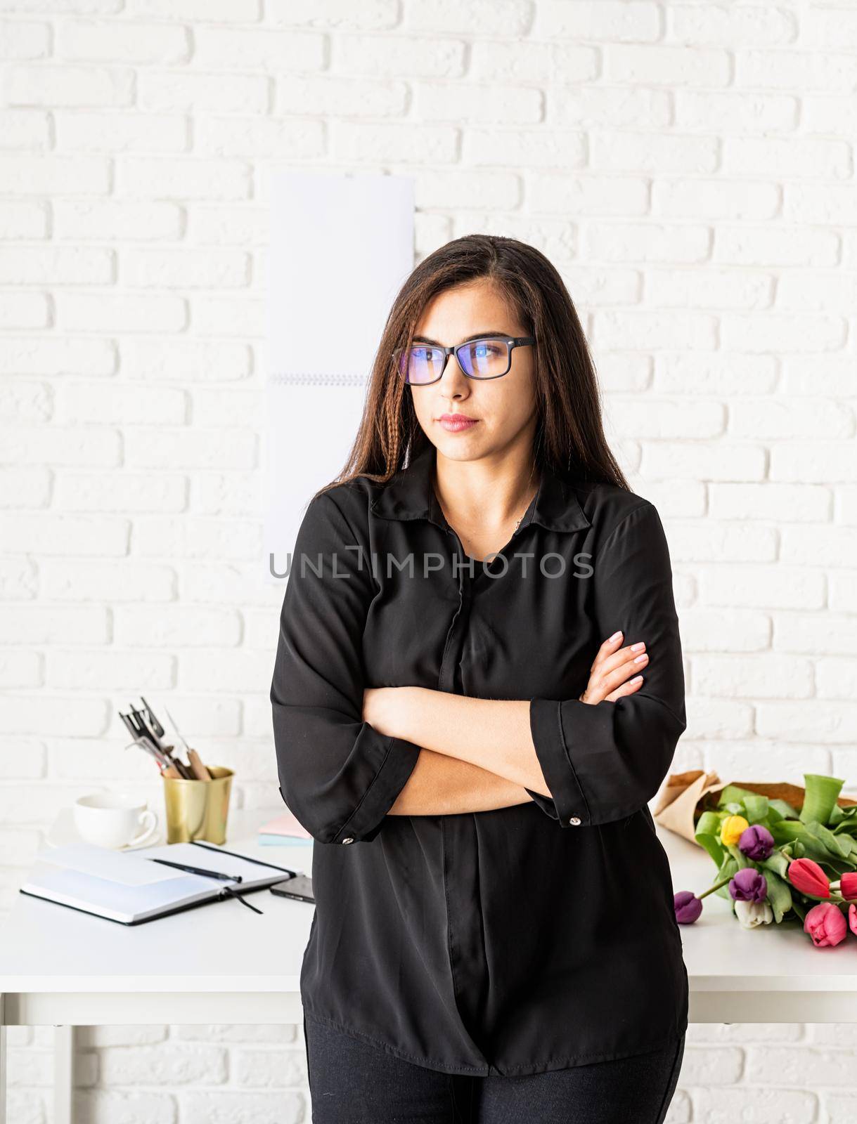 Small business concept. Portrait of young confident brunette business woman working at the office, standing by the desk with arms crossed