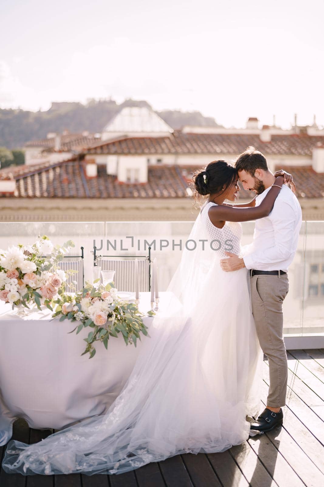 Interracial wedding couple. Destination fine-art wedding in Florence, Italy. African-American bride and Caucasian groom stand near the table for a wedding dinner. by Nadtochiy