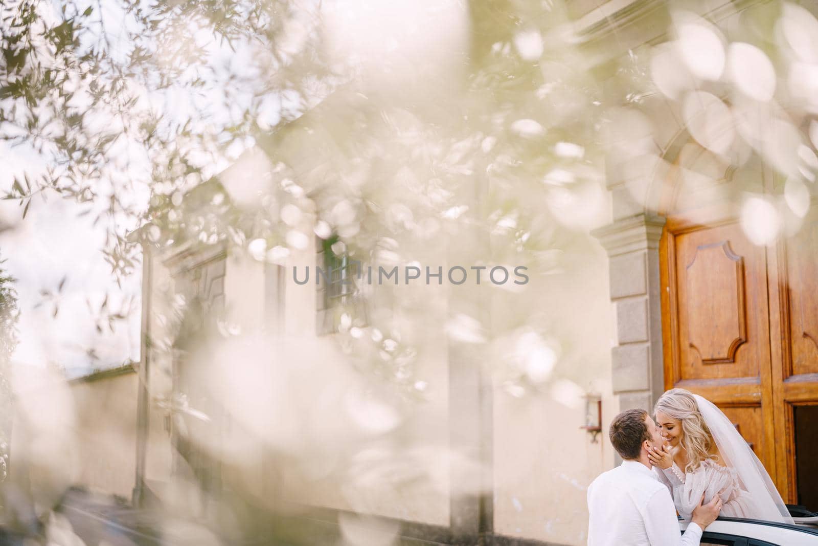 The bride looks out of the cabriolet and kisses the groom. Wedding in Florence, Italy, in an old villa-winery. by Nadtochiy