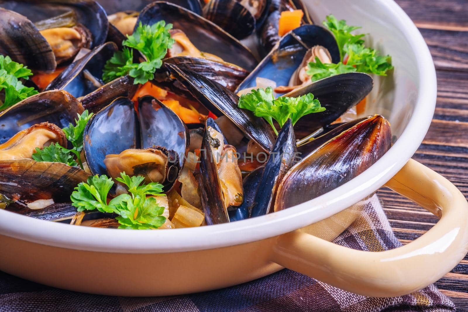 Boiled mussels in cooking dish with parsley on a wooden background by Fischeron