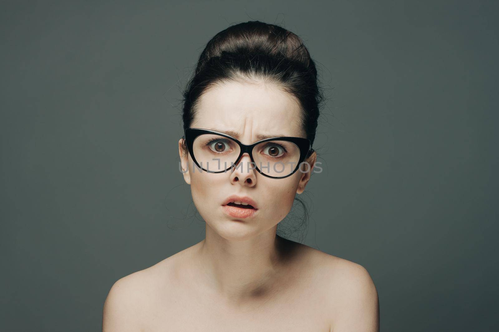 woman with glasses naked shoulders gathered hair gray background. High quality photo