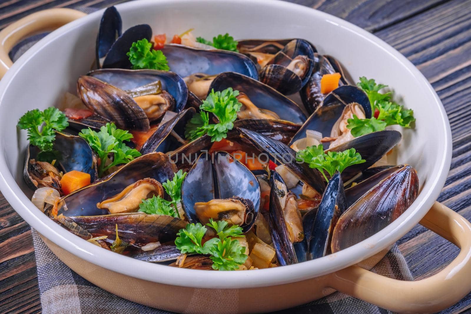 Boiled mussels in cooking dish with parsley on dark wooden background