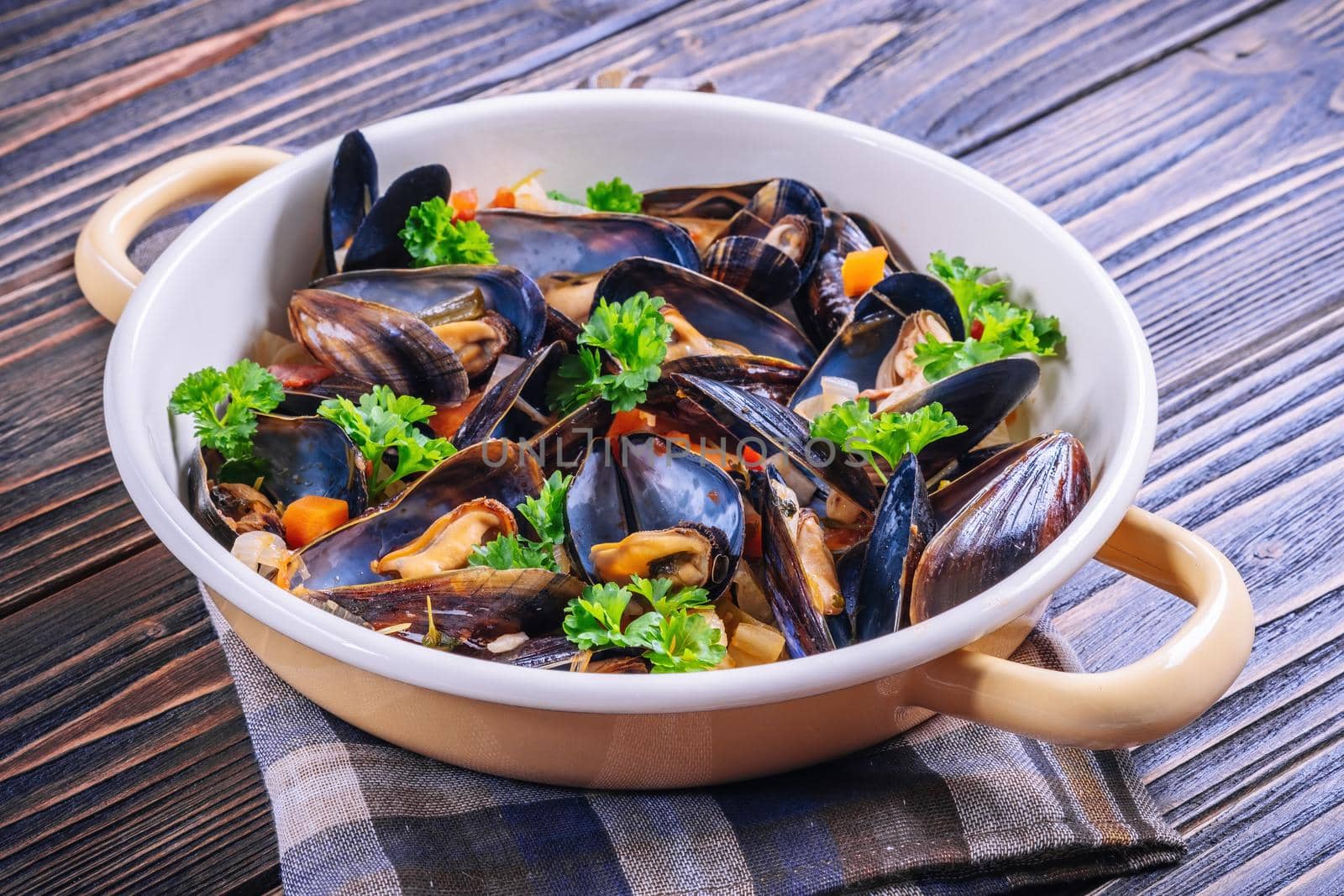 Boiled mussels in cooking dish with parsley on dark wooden background