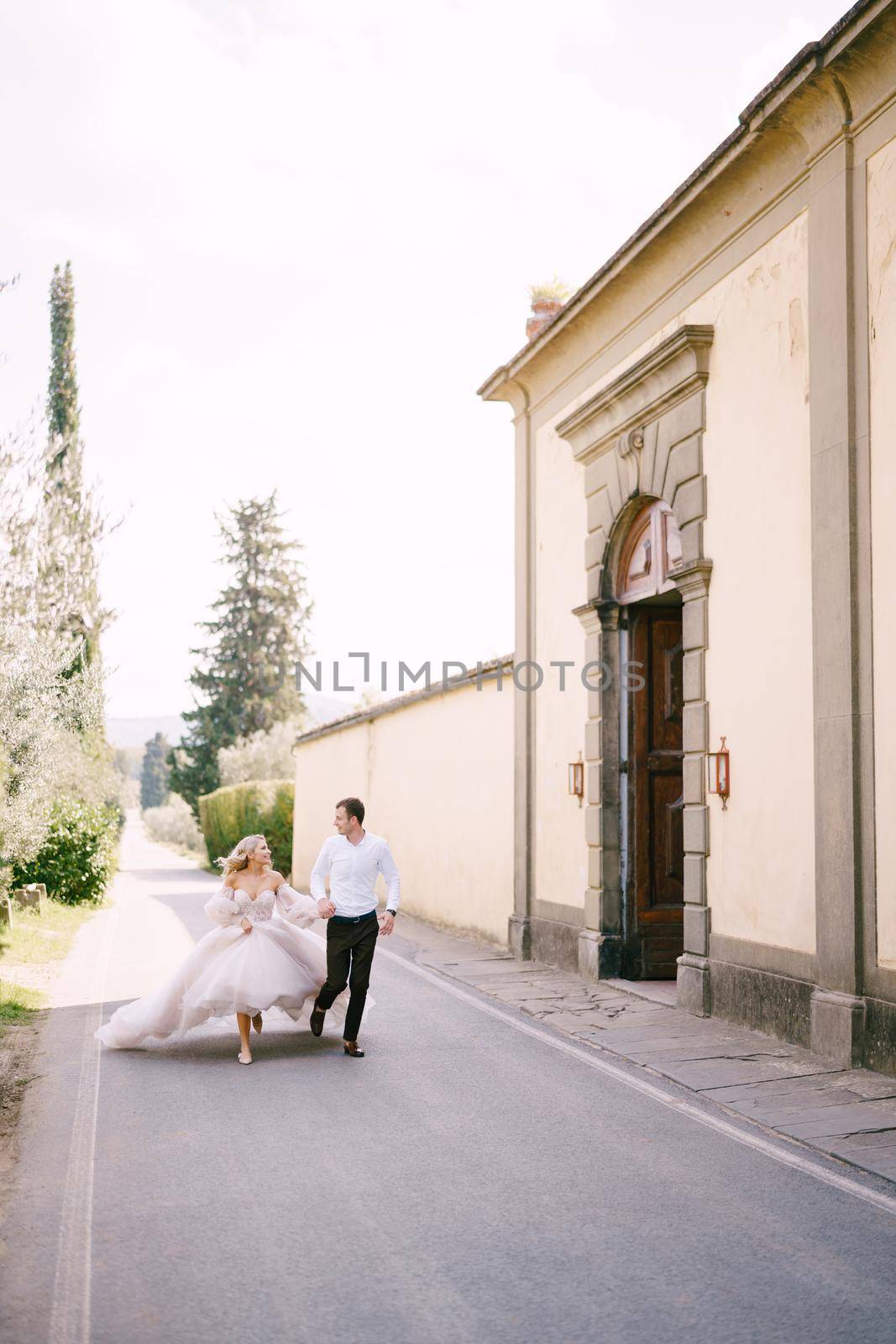 Beautiful bride and groom running hand in hand outside of the old villa in Italy, in Tuscany, near Florence.