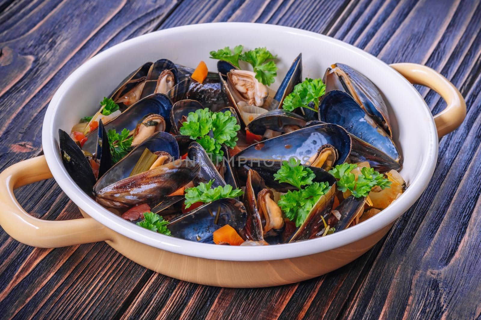 Boiled mussels in cooking dish with parsley on a wooden background by Fischeron