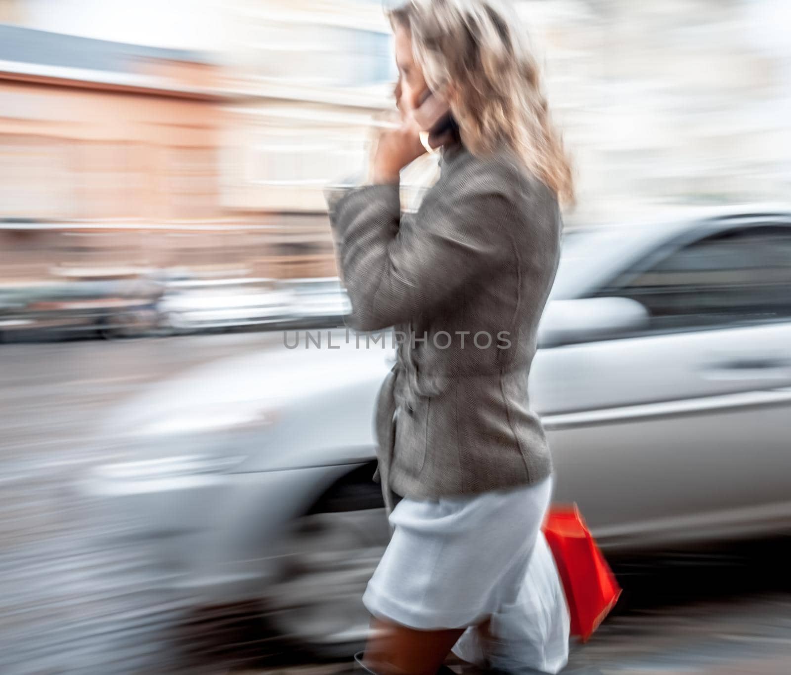 Abstract image of a young woman talking on a mobile phone on a city background with car. Intentional motion blur