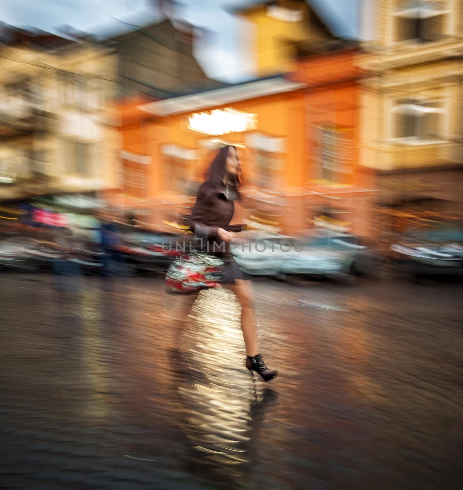 Abstract image of a woman walking down the street after a rain. Intentional motion blur