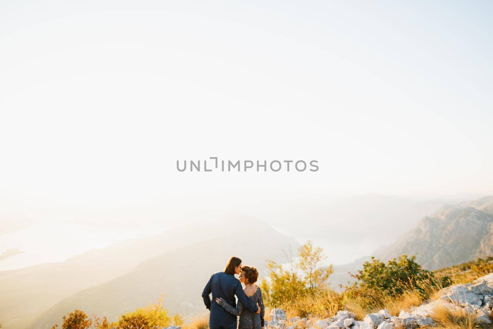 The bride and groom embracing and kissing on the Lovcen mountain behind them opens a view of the Bay of Kotor, back view . High quality photo