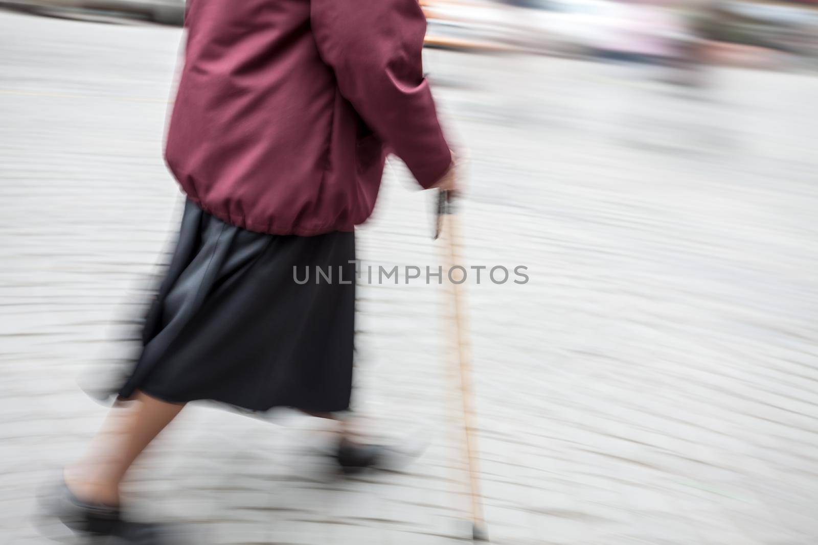 Elderly sick woman with a cane walking down the street. Intentional motion blur