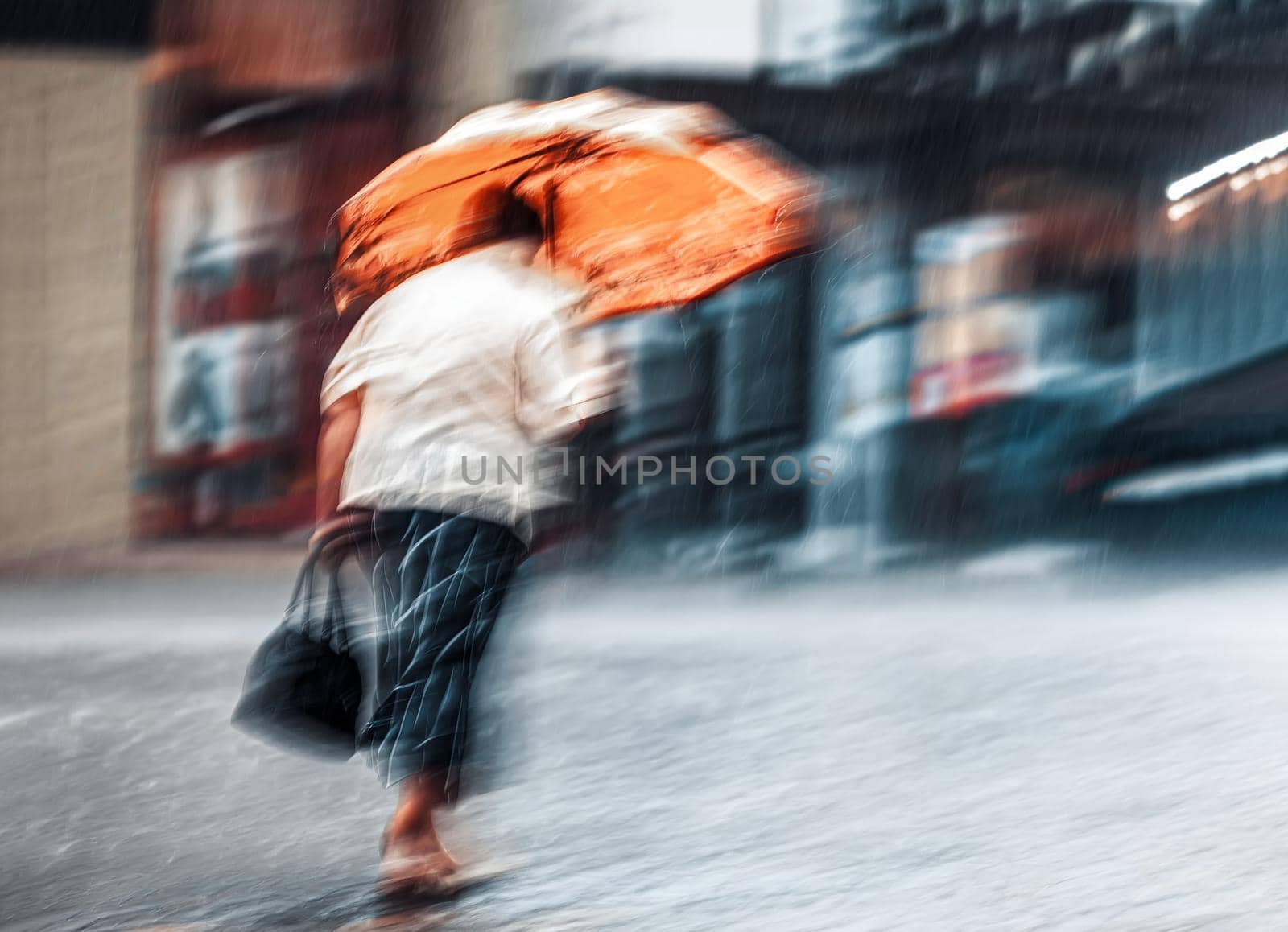Intentional motion blur image with lonely woman with orange umbrella walking down the street in rainy day. 