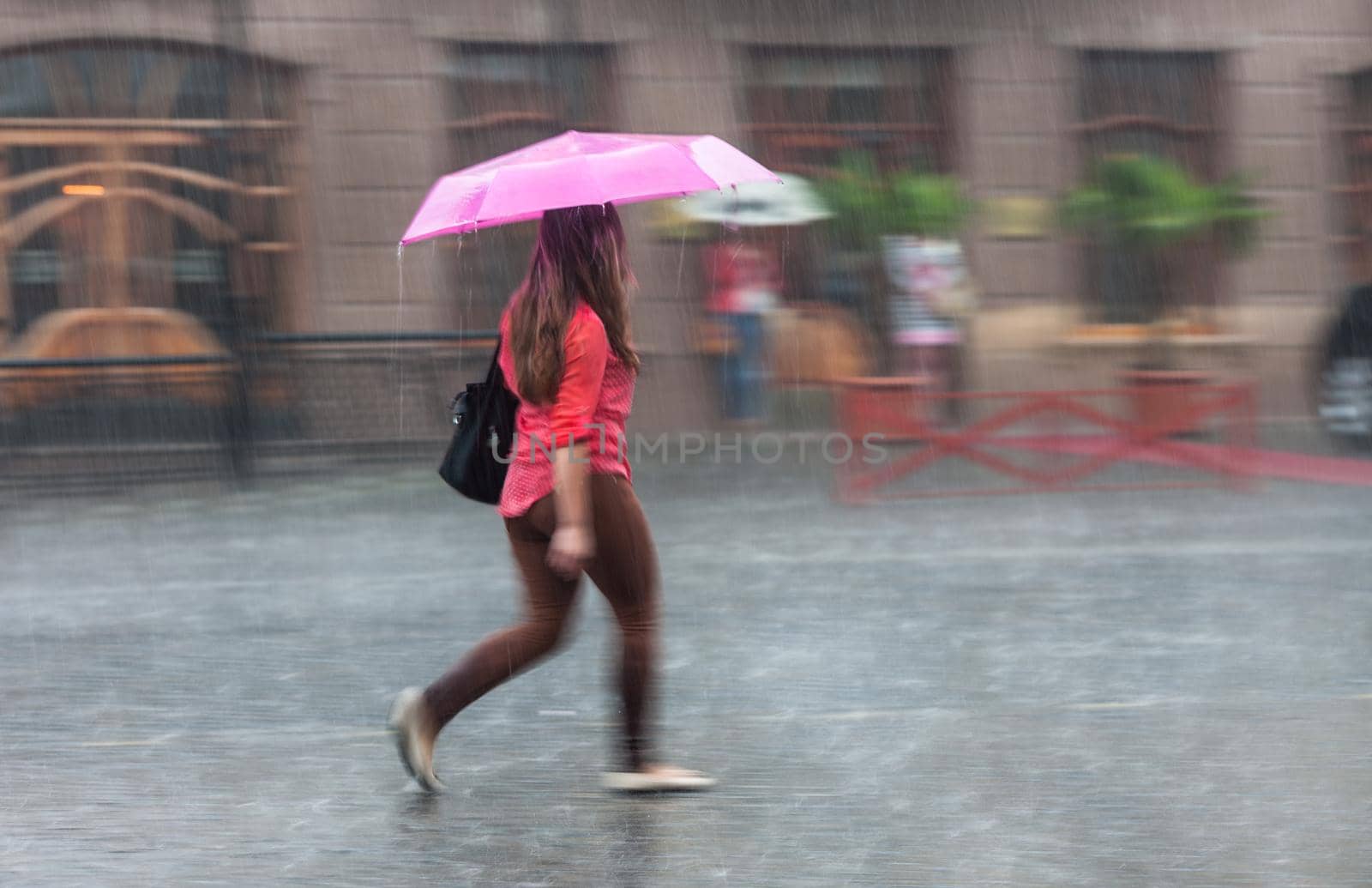 Shower. Woman walking down the street in rainy day. Intentional motion blur
