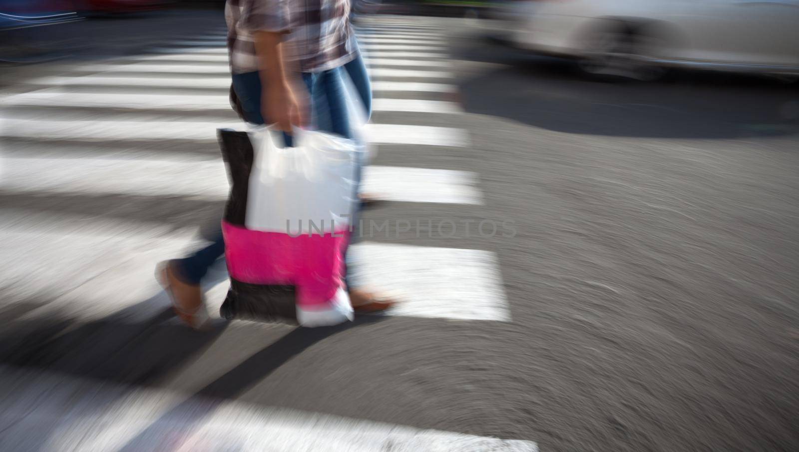 Woman with shopping bag crossing the street at a crosswalk. Intentional motion blur