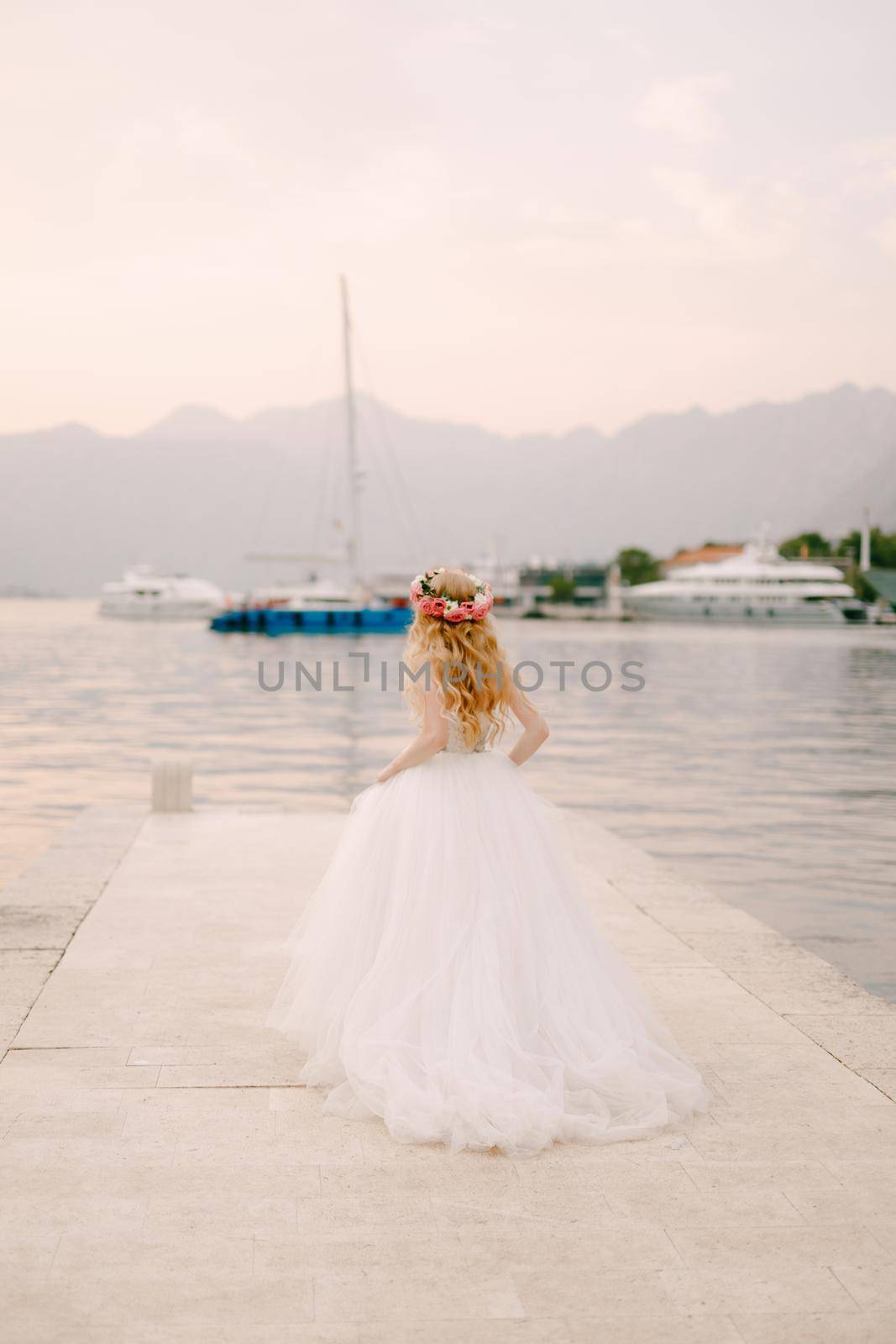 A bride in a delicate wreath of roses stands on a pier near Kotor in the Bay of Kotor, back view . High quality photo