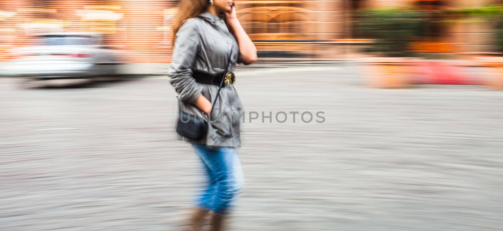 Abstract image of a young woman talking on a mobile phone on a city background with car. Intentional motion blur