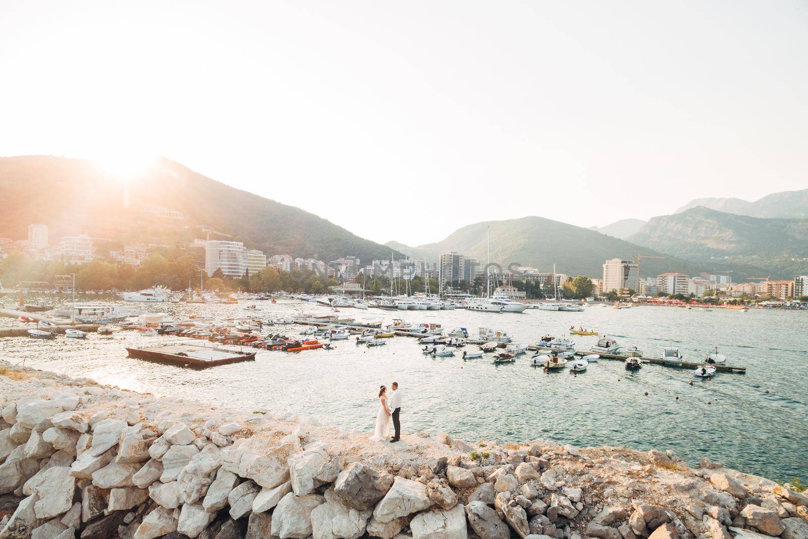 The bride and groom hold hands against the background of the boat pier in Budva . High quality photo