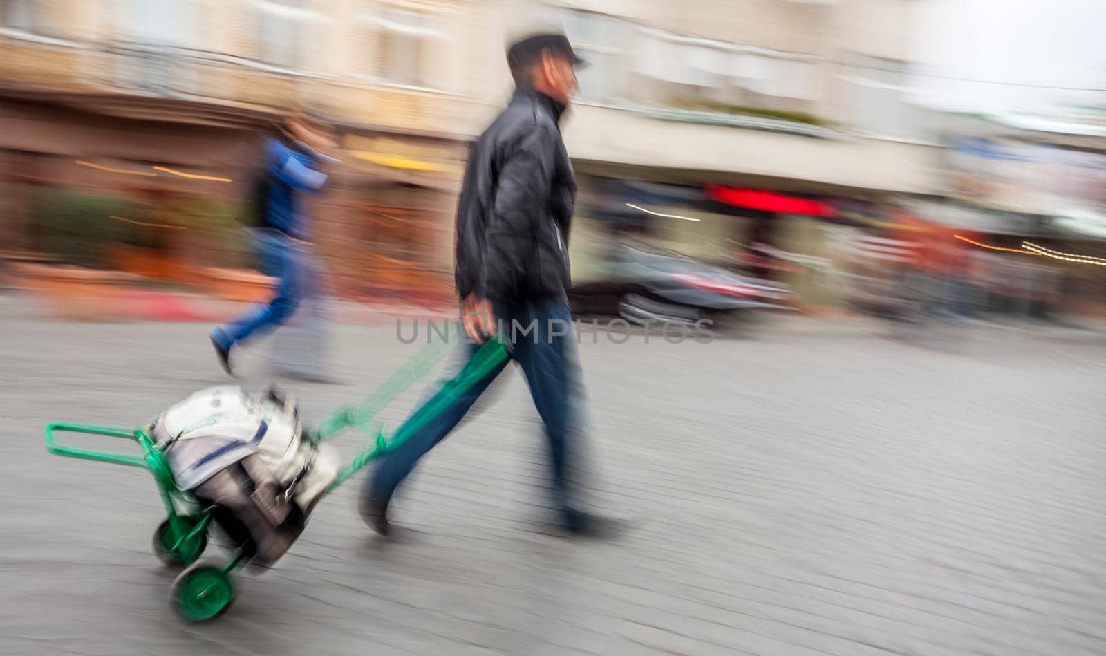 Middle-aged man carries the cart with bag. Intentional motion blur