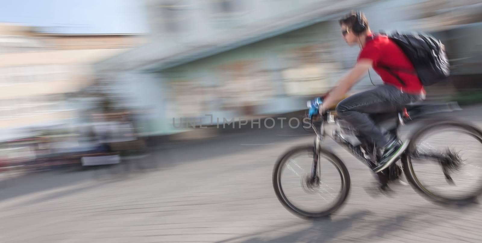 Young man with headphones and backpack riding a bicycle on the street. Intentional motion blur