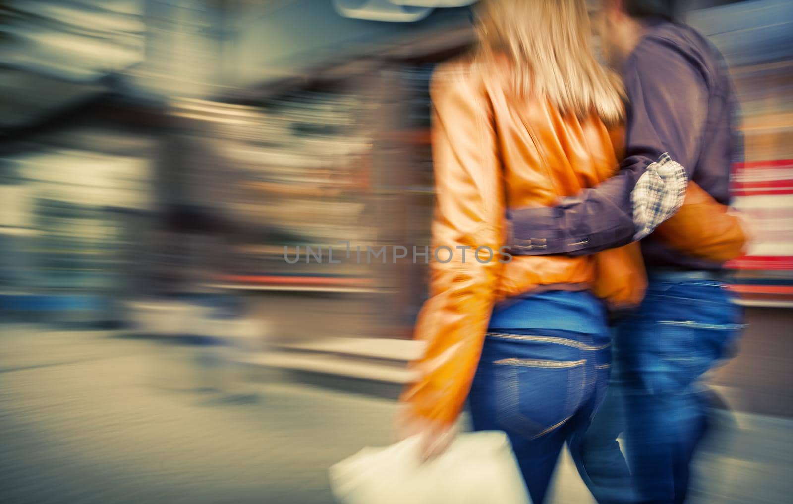 Man in jeans and a woman in a leather jacket walking down the street hugging. Intentional motion blur and color shift