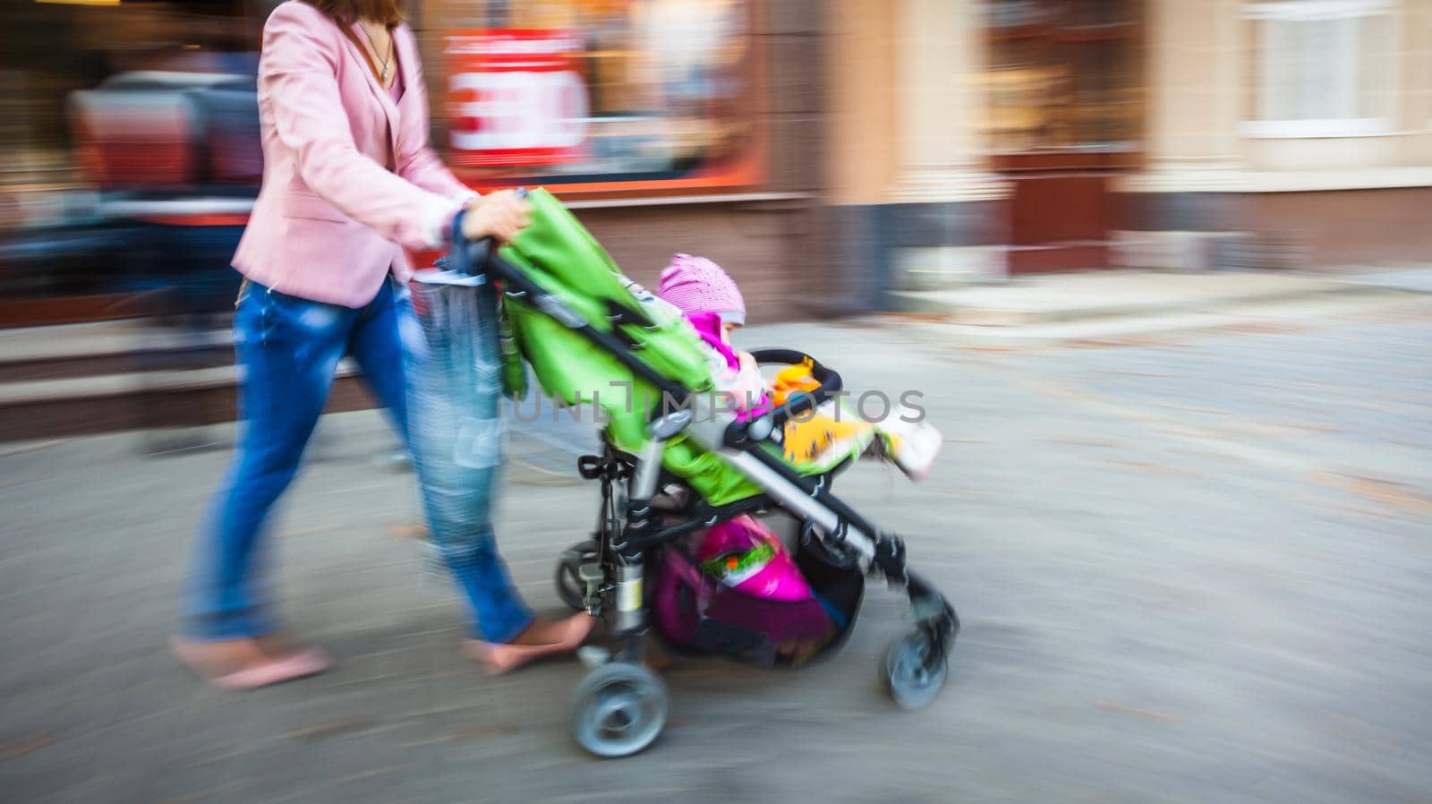 Mother with small child and a pram walking down the street. Intentional motion blur