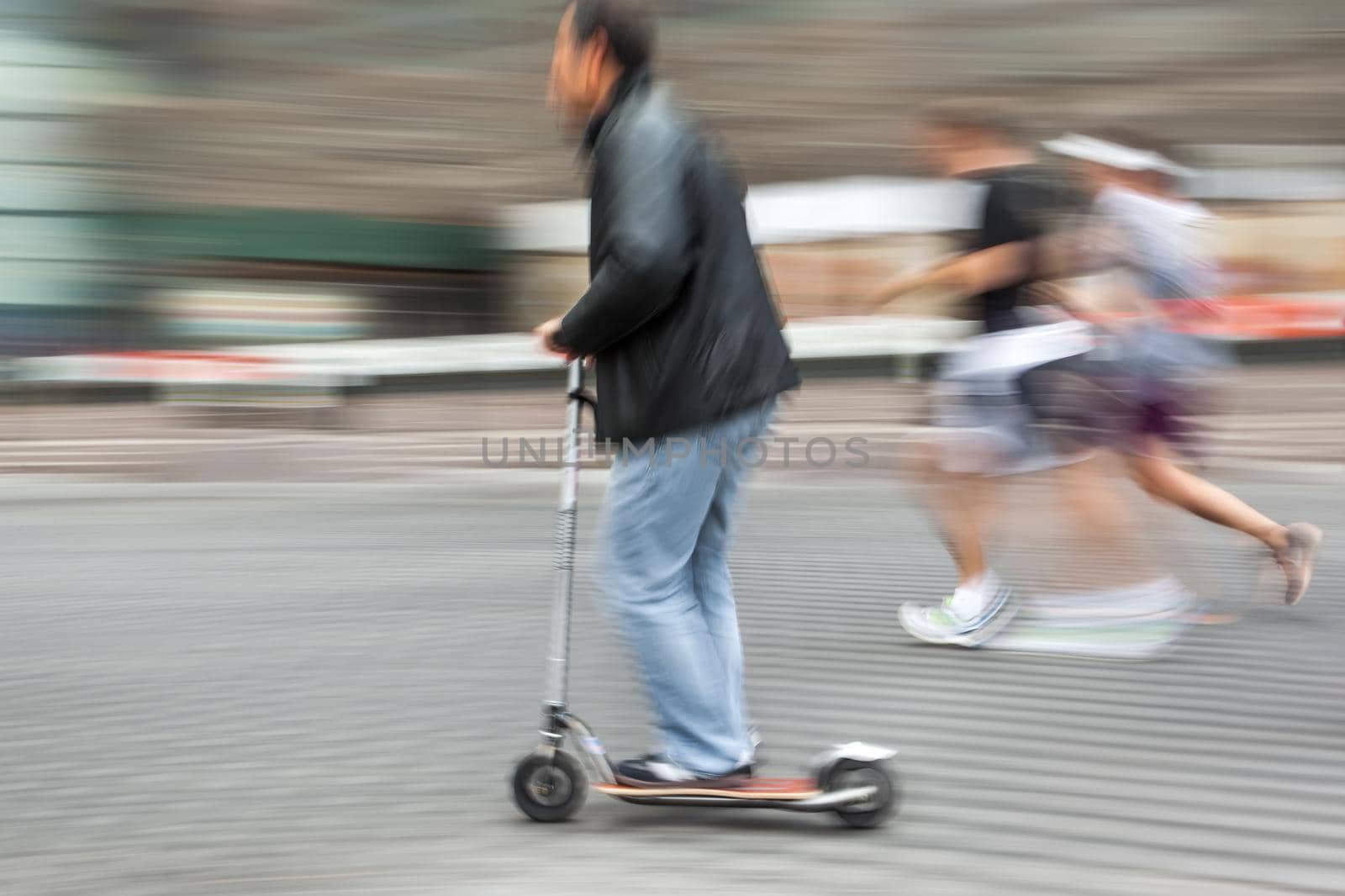 Man on a scooter and a pair running down the street. Intentional motion blur and color shift
