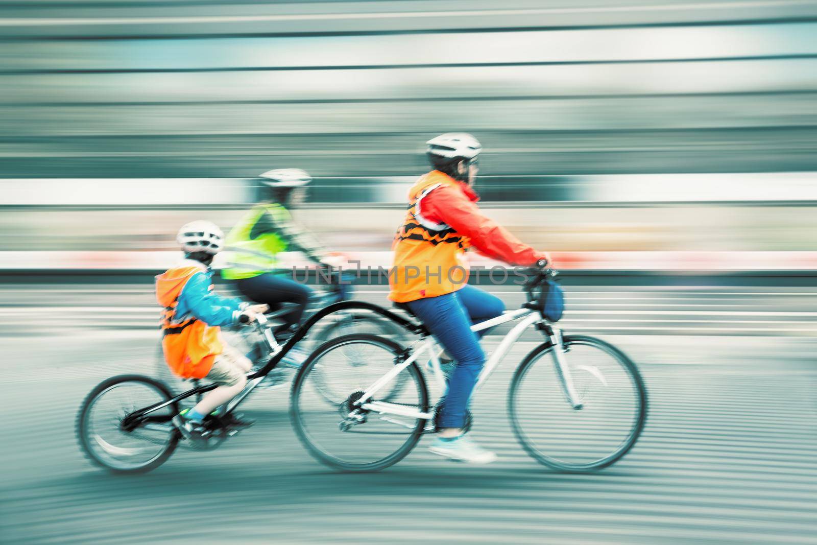 Young family with a child ride a bikes on a city streets. Intentional motion blur and color shift