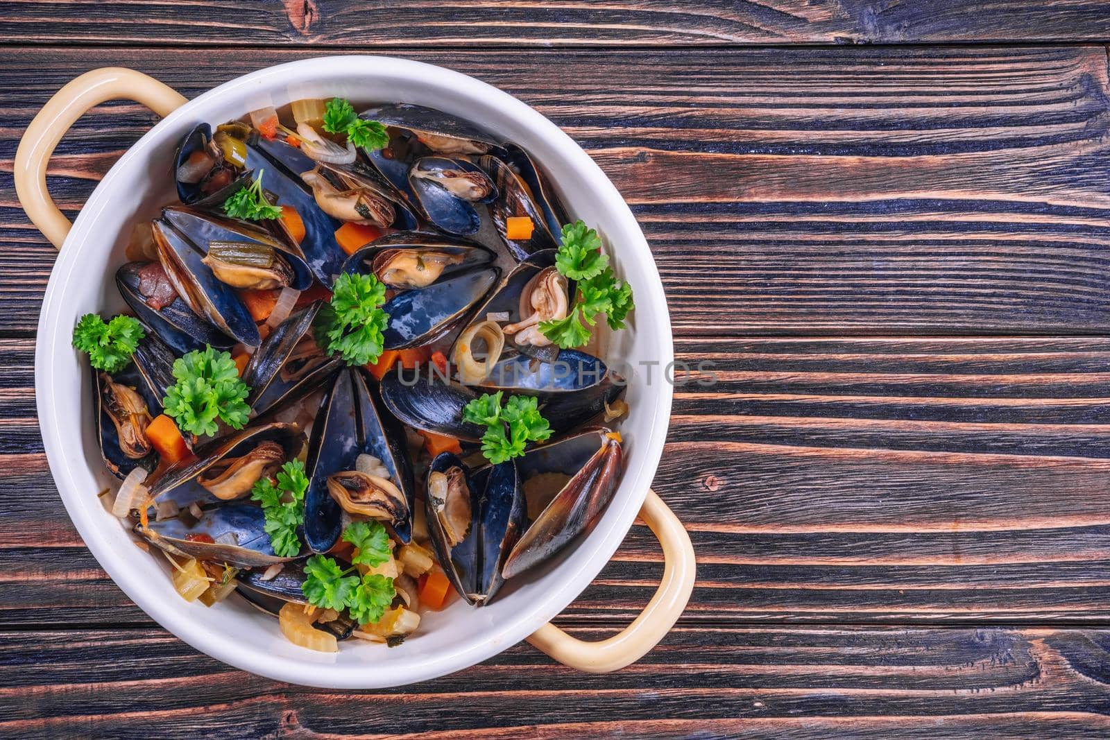 Boiled mussels in cooking dish with parsley on dark wooden background