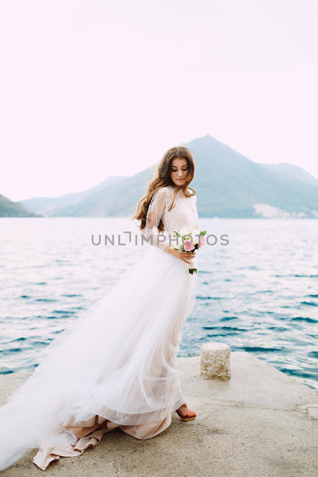 The bride holds a bouquet of roses in her hands and stands on the pier in the Bay of Kotor. High quality photo