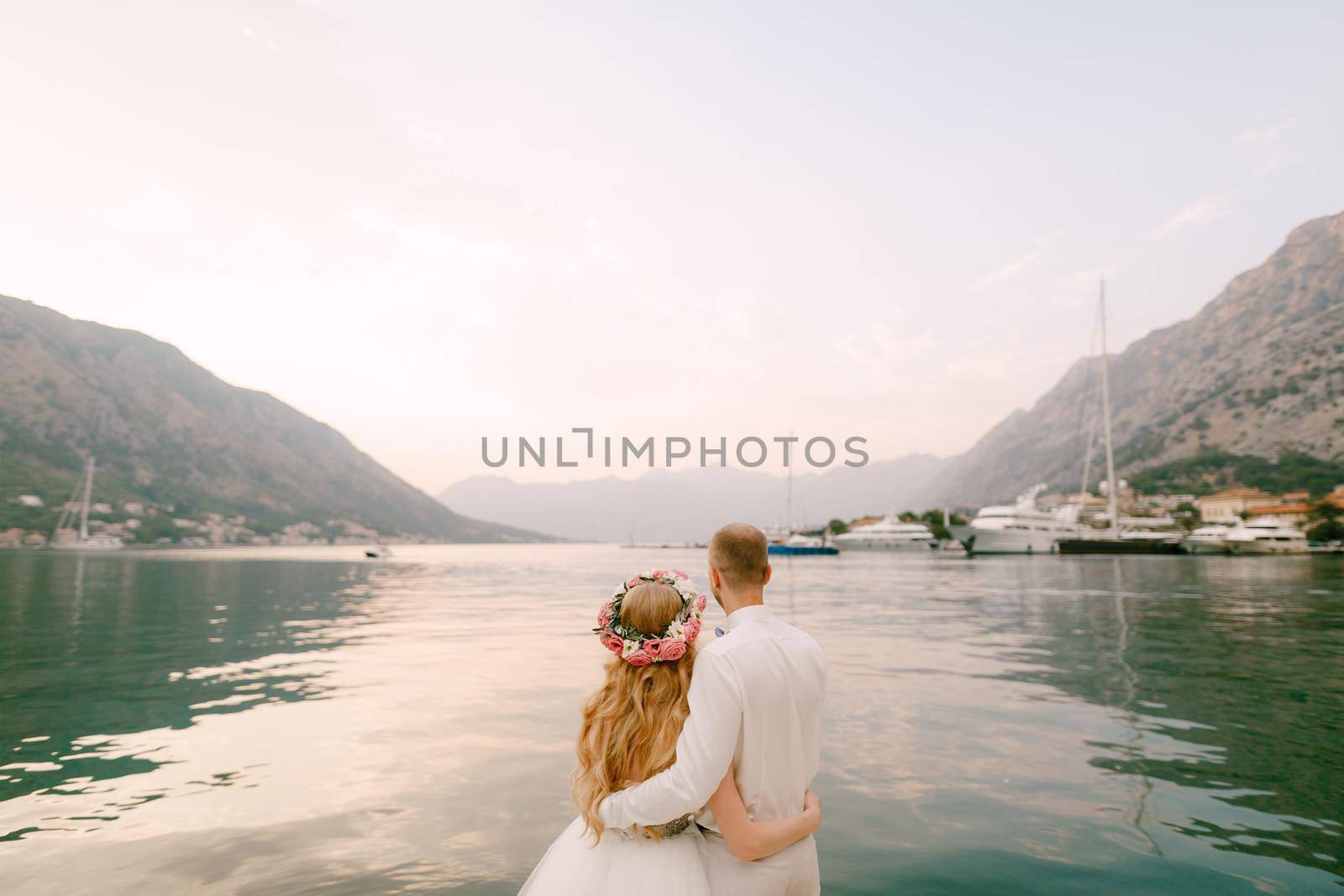 The bride in a wreath and groom hug on the pier near the old town of Kotor in the Bay of Kotor, close-up. High quality photo