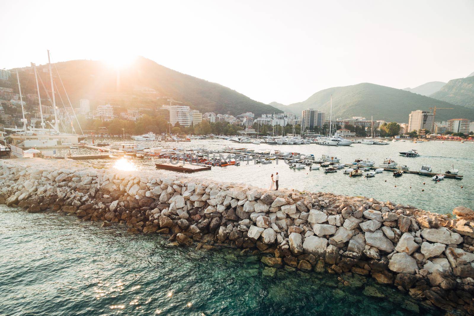 The bride and groom hold hands against the background of the boat pier in Budva . High quality photo