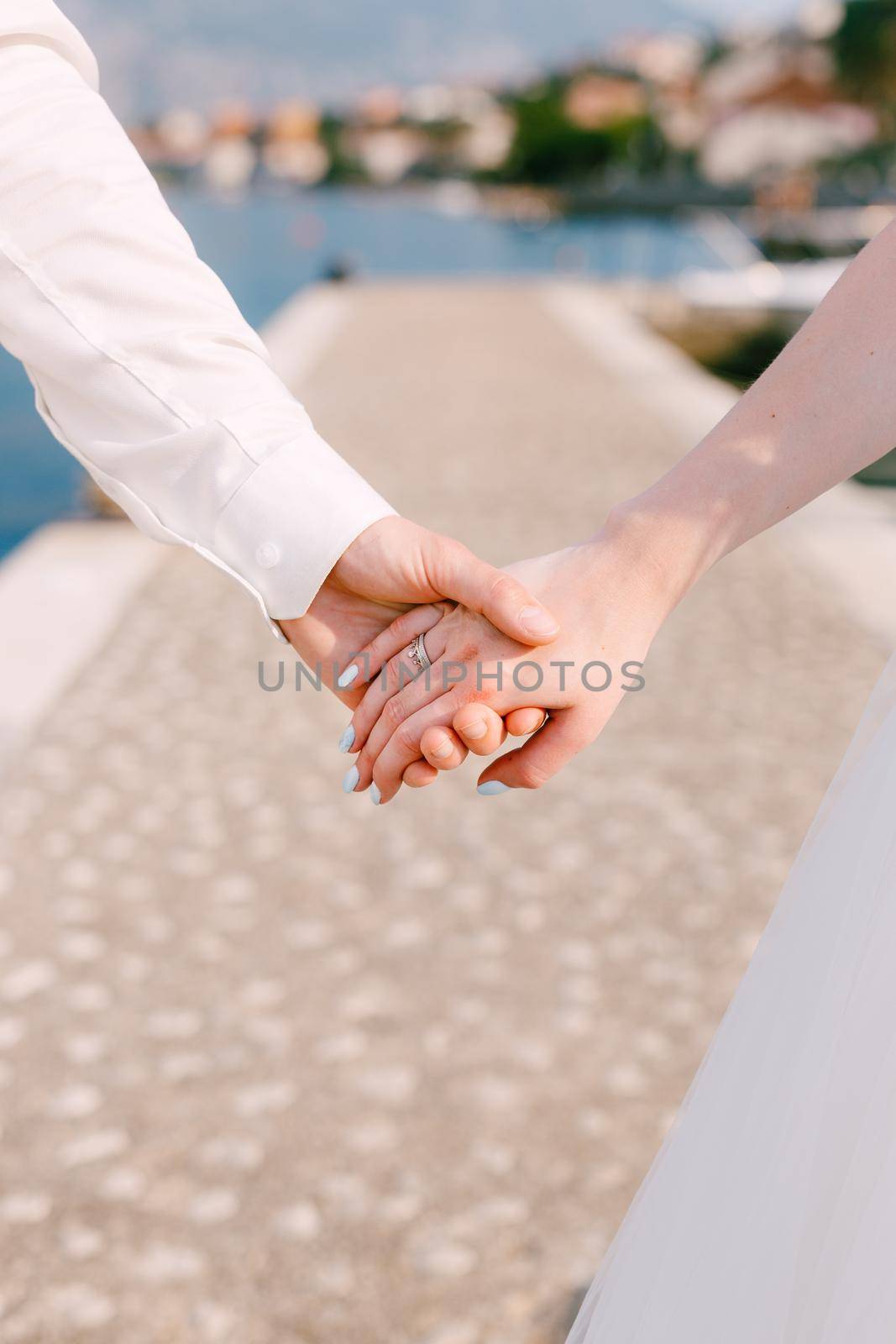 Bride's hand with a wedding ring on the finger in the groom's hand, close-up on a pier in the Bay of Kotor . High quality photo