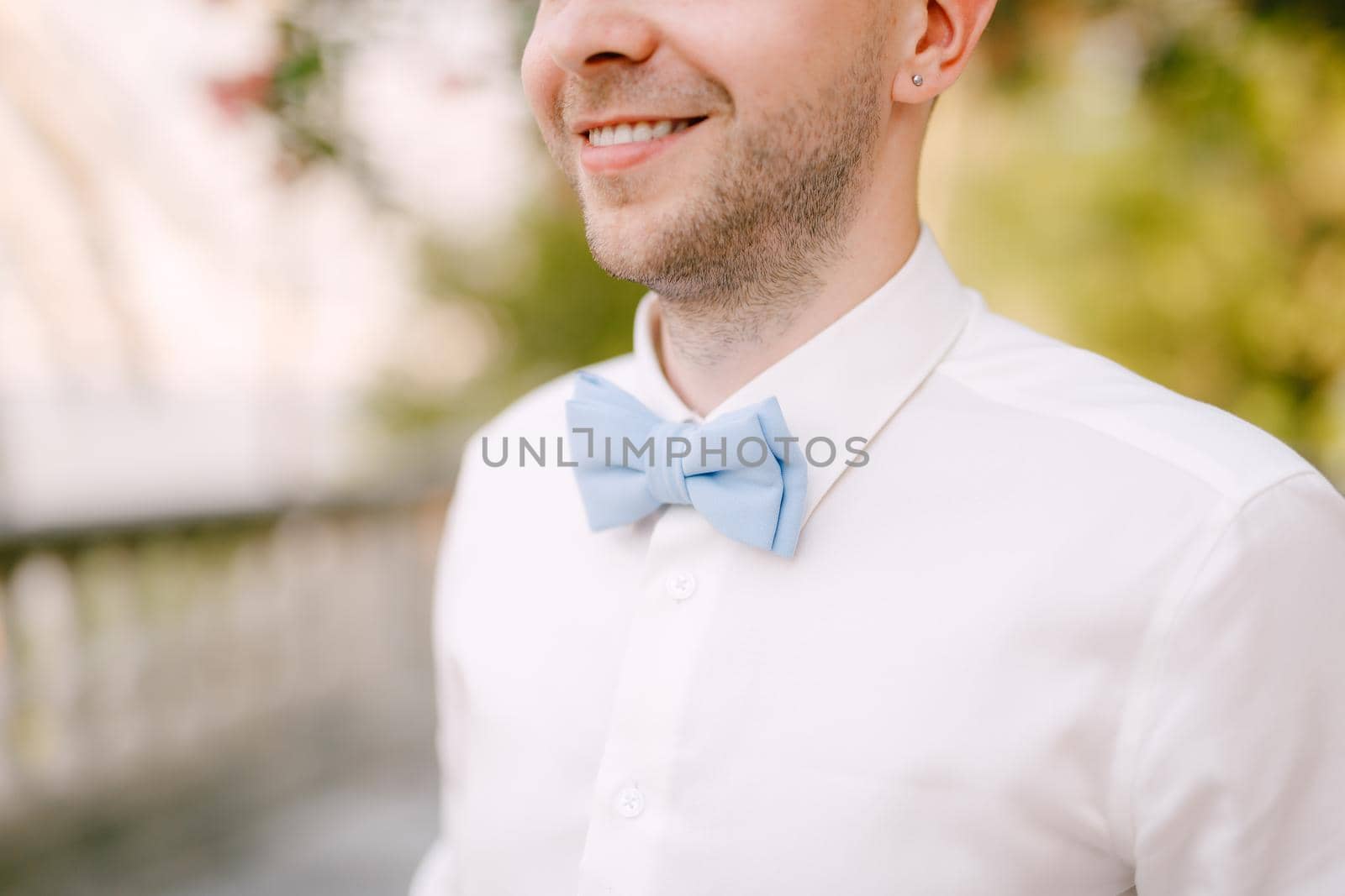 A man in a white shirt and a blue bow tie smiles on a sunny day, close-up . High quality photo