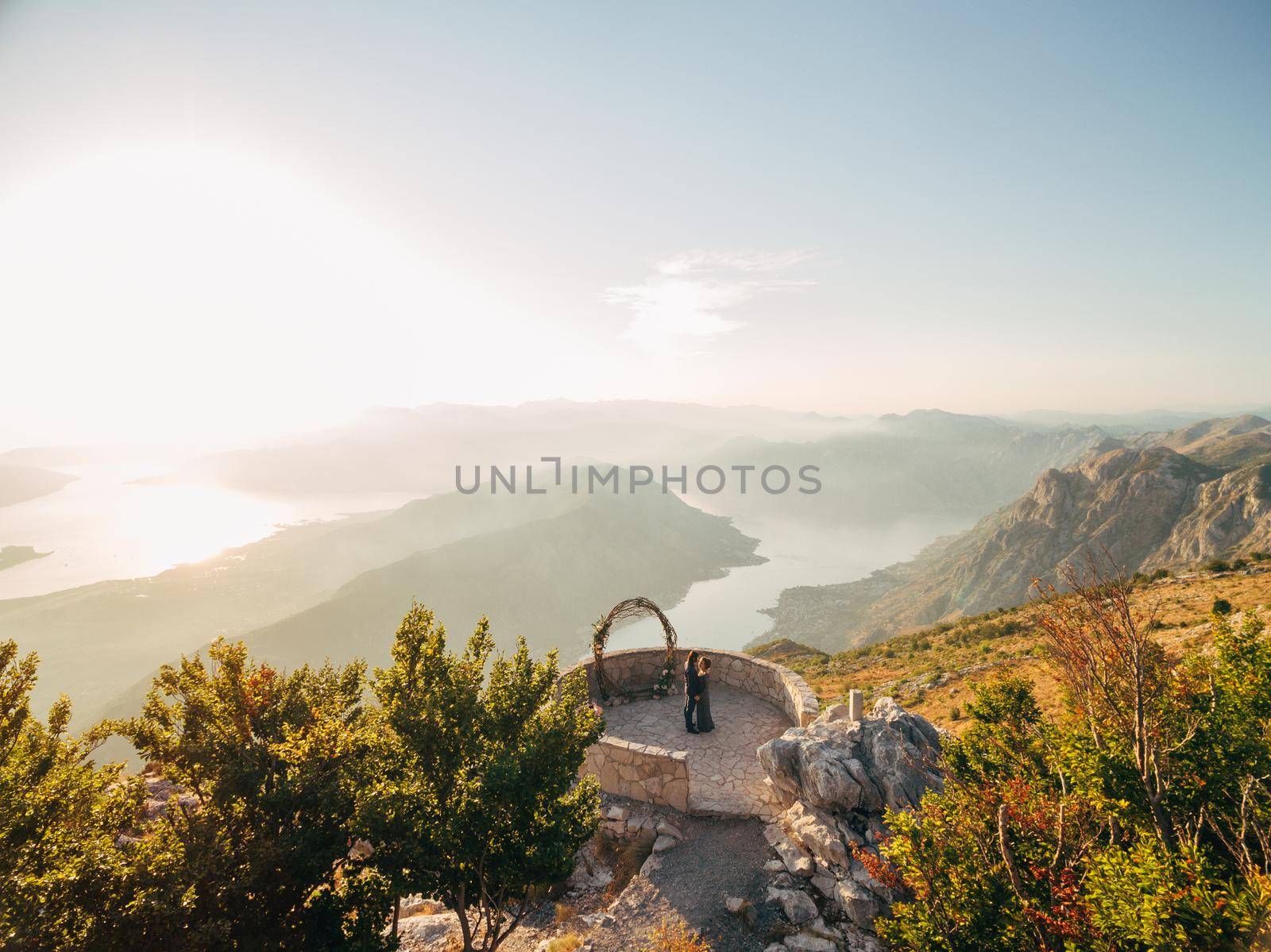 The bride and groom hug near the wedding arch on the observation deck on Mount Lovcen overlooking the Bay of Kotor . High quality photo