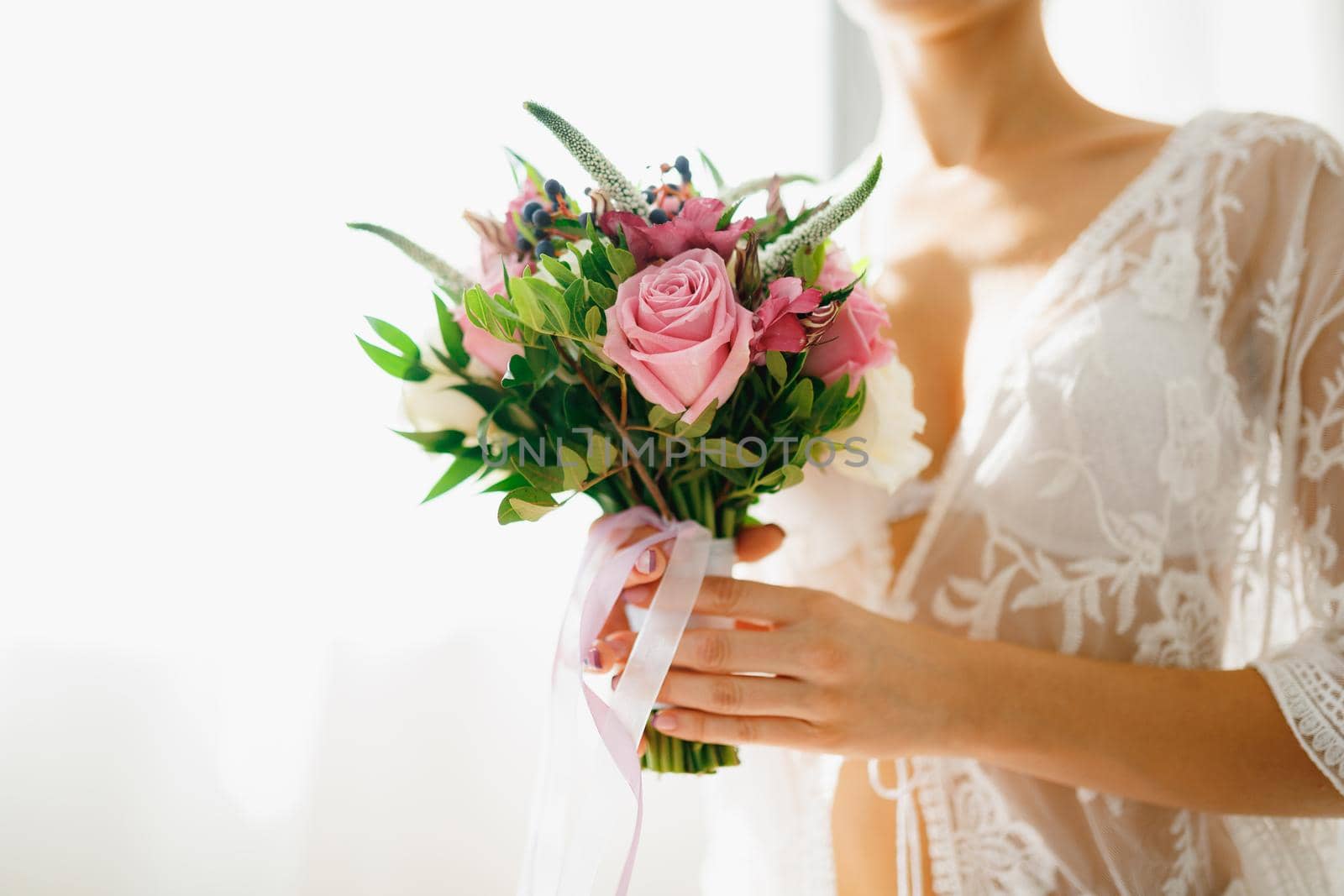 A bride in a white lace peignoir holds a wedding bouquet in her hands in a hotel room while preparing for a wedding ceremony . High quality photo