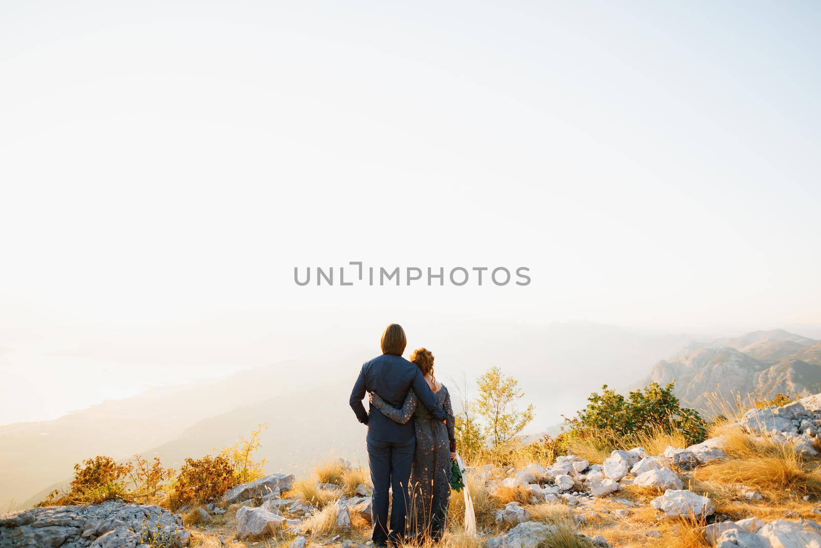 The bride and groom embracing on the Lovcen mountain behind them opens a view of the Bay of Kotor, back view by Nadtochiy