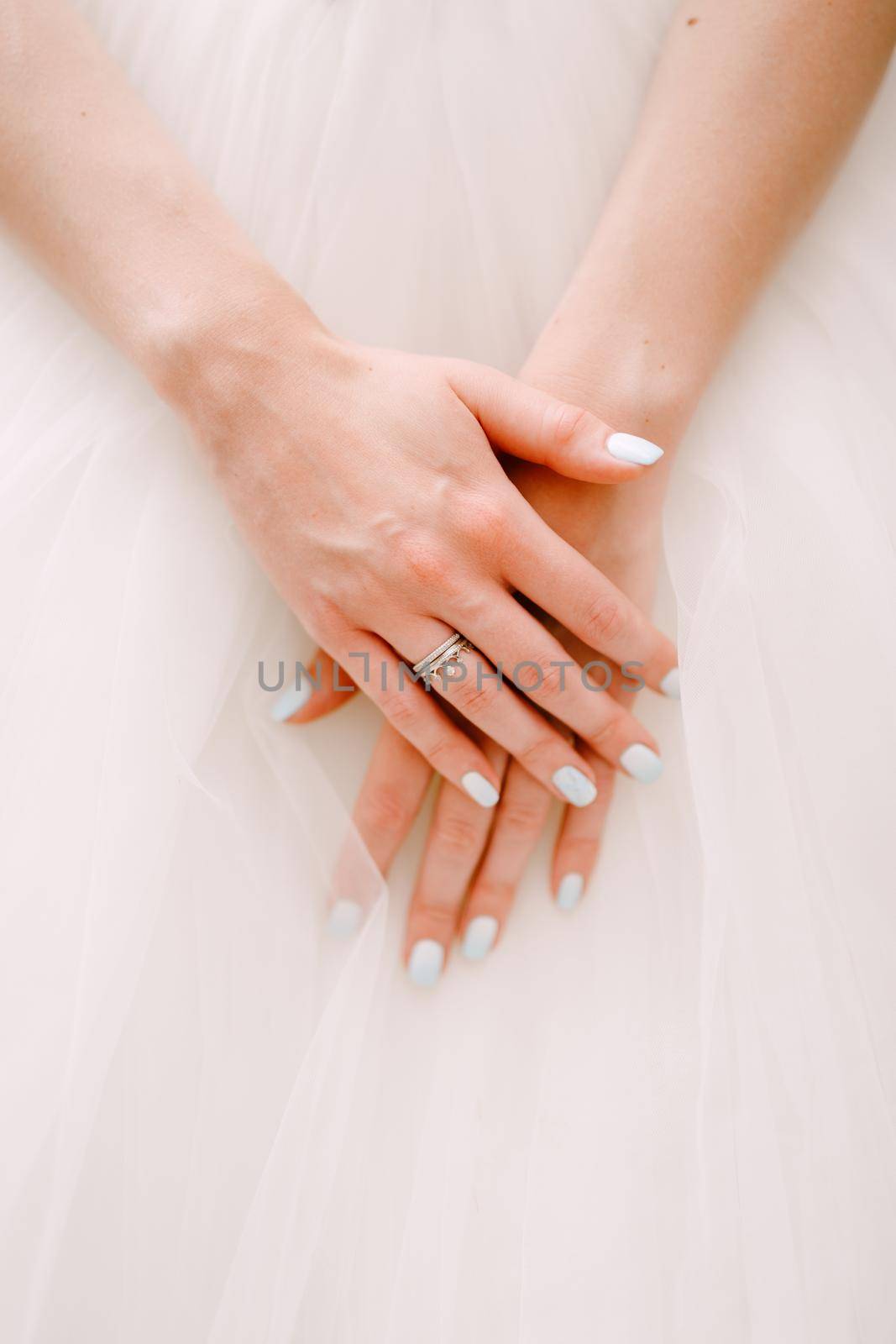 Graceful hands of the bride folded on a fluffy skirt of a wedding dress, close-up . High quality photo