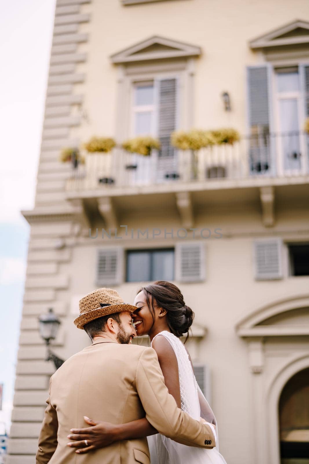Wedding in Florence, Italy. Multiracial wedding couple. African-American bride in a white dress with a long veil and a bouquet, and Caucasian groom in a sandy jacket and straw hat. by Nadtochiy