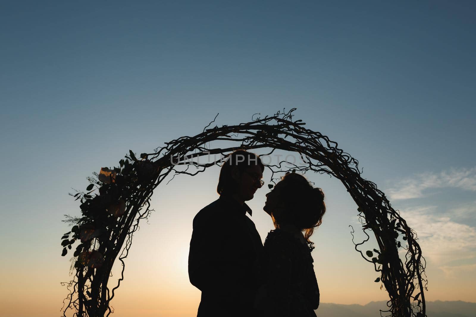 Silhouettes of hugging bride and groom near the wedding arch at sunset at the wedding ceremony. High quality photo