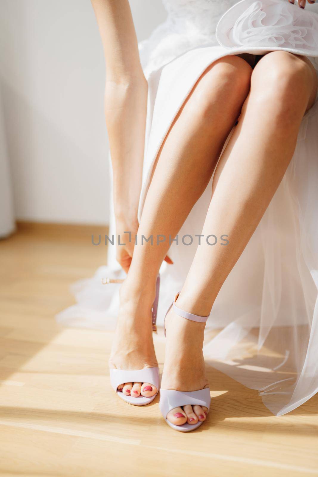 The bride sitting in a chair in a hotel room and putting on sandals during wedding preparations, close-up. High quality photo