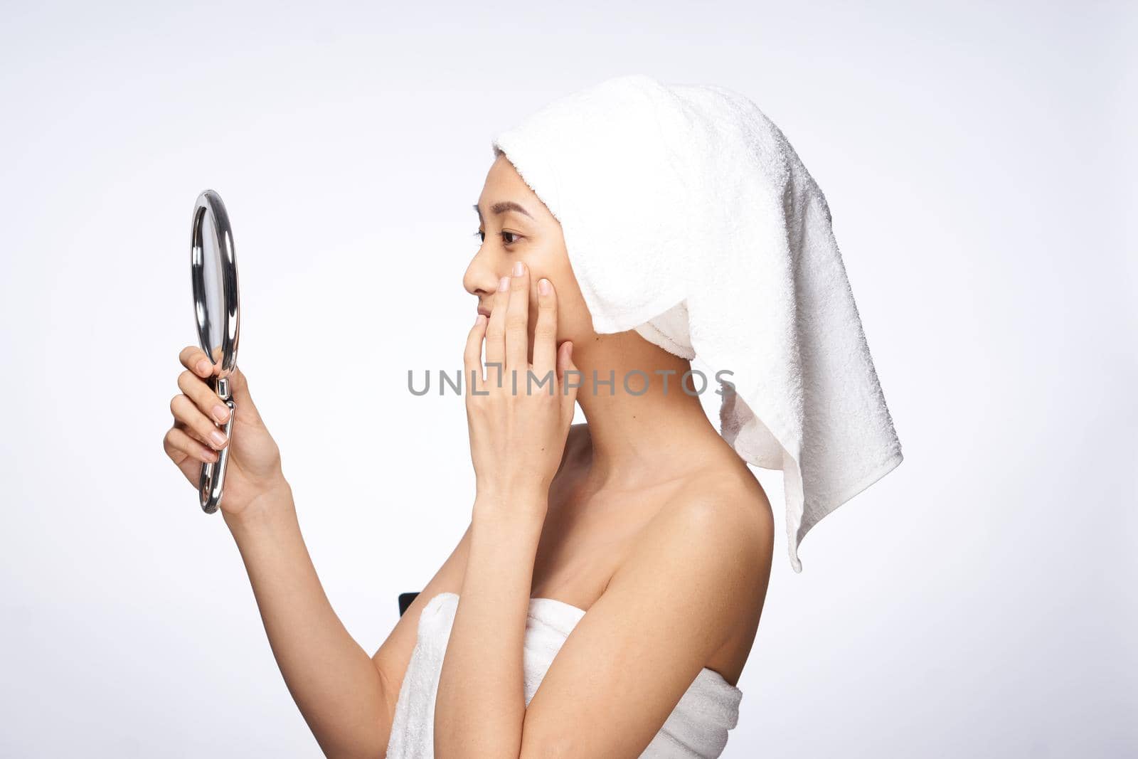 woman of asian appearance after shower looks in the mirror skin care light background. High quality photo