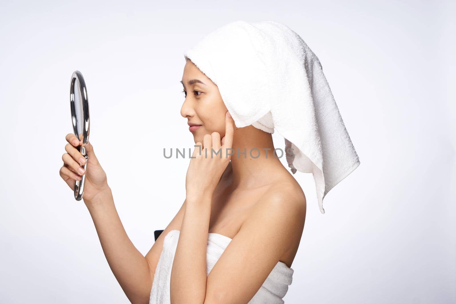 woman of asian appearance after shower looks in the mirror skin care light background. High quality photo