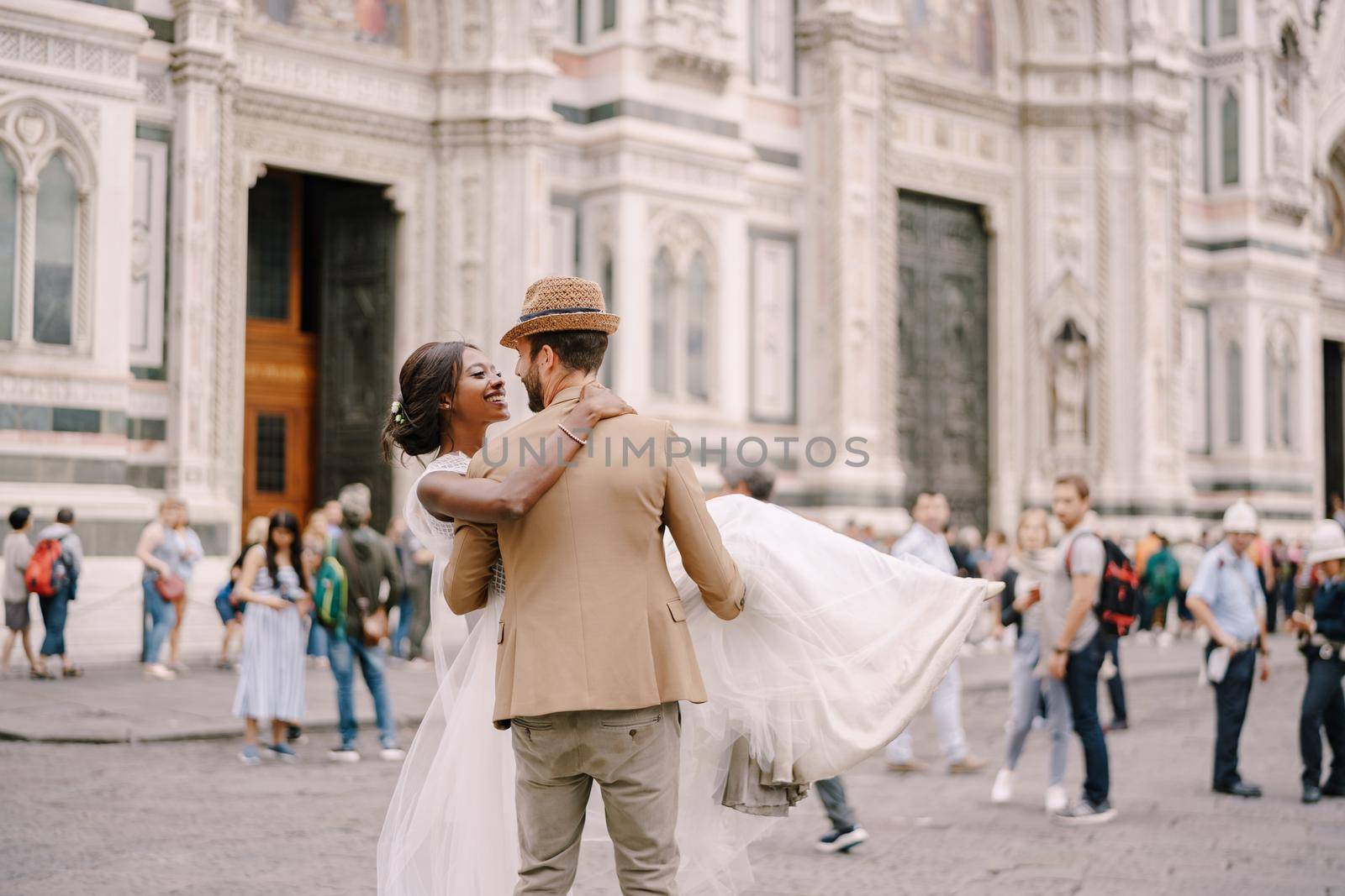 Caucasian groom circles and kisses African-American bride in Piazza del Duomo. Wedding in Florence, Italy. Mixed-race wedding couple
