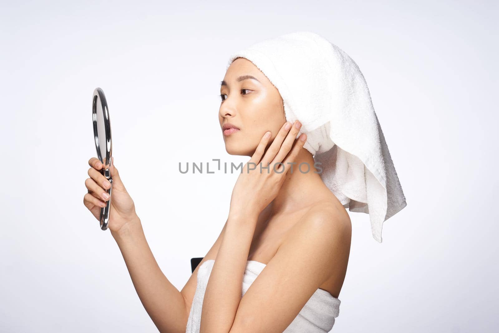 woman of asian appearance after shower looks in the mirror skin care light background. High quality photo