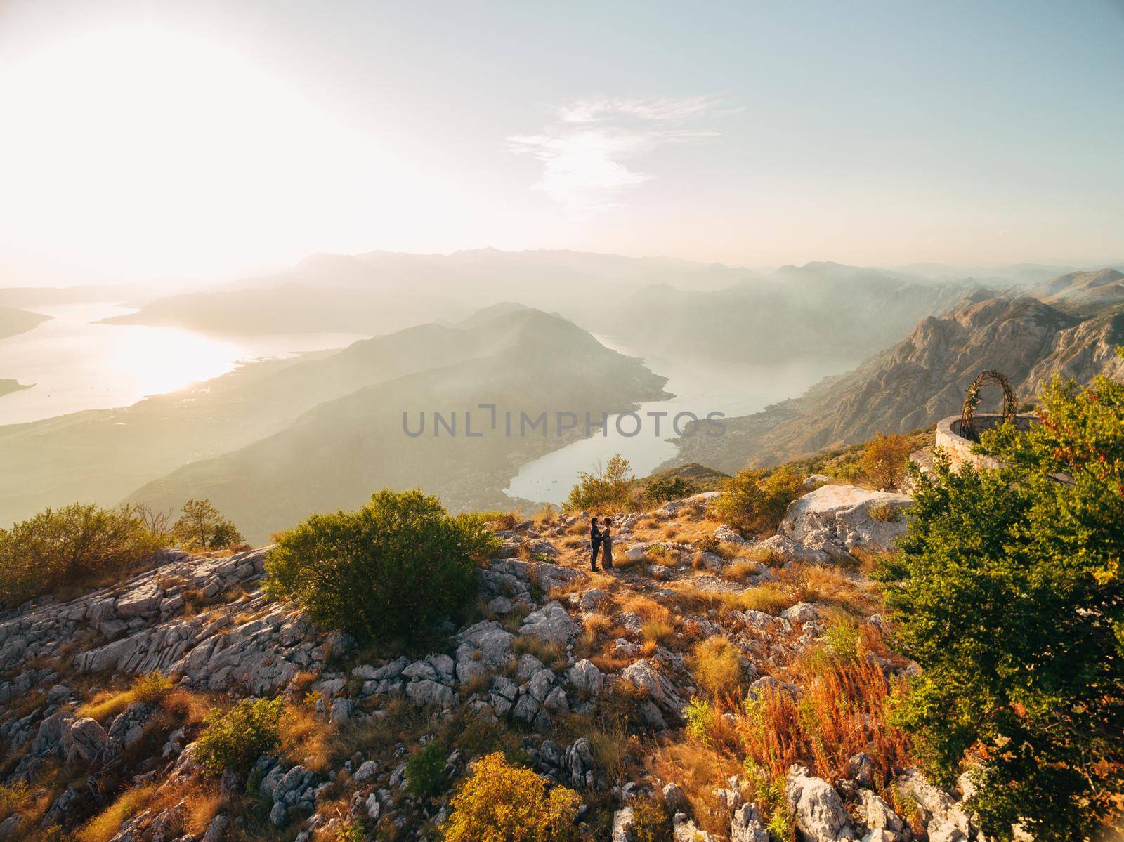 The bride and groom embracing on the Lovcen mountain behind them opens a view of the Bay of Kotor by Nadtochiy