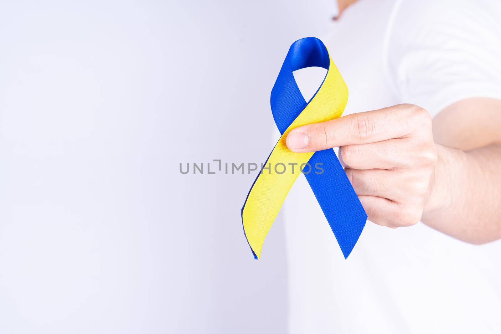 Down syndrome day, hands holding blue yellow ribbon awareness on chest support patient with illness disability