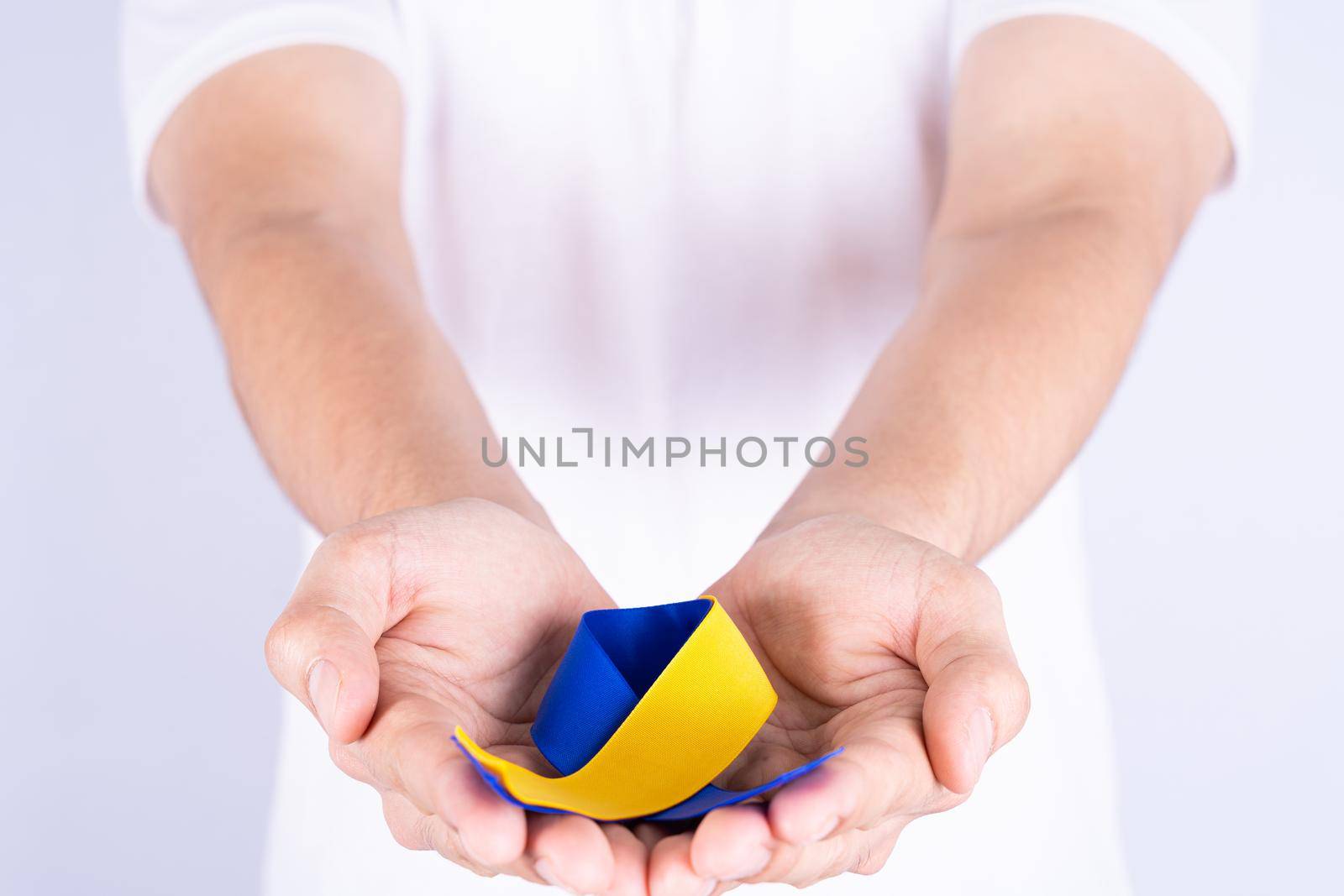 Down syndrome day, hands holding blue yellow ribbon awareness support patient with illness disability by mikesaran