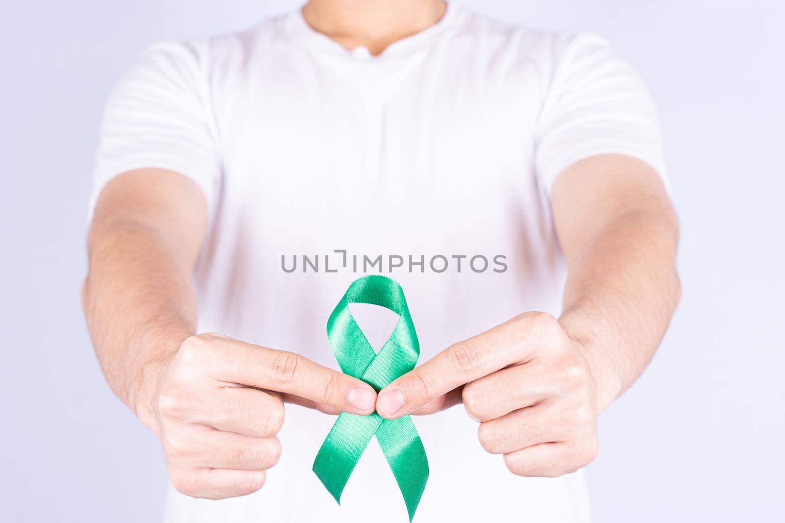 World kidney day, hands holding green ribbon awareness of kidney disease on chest isolated grey background.