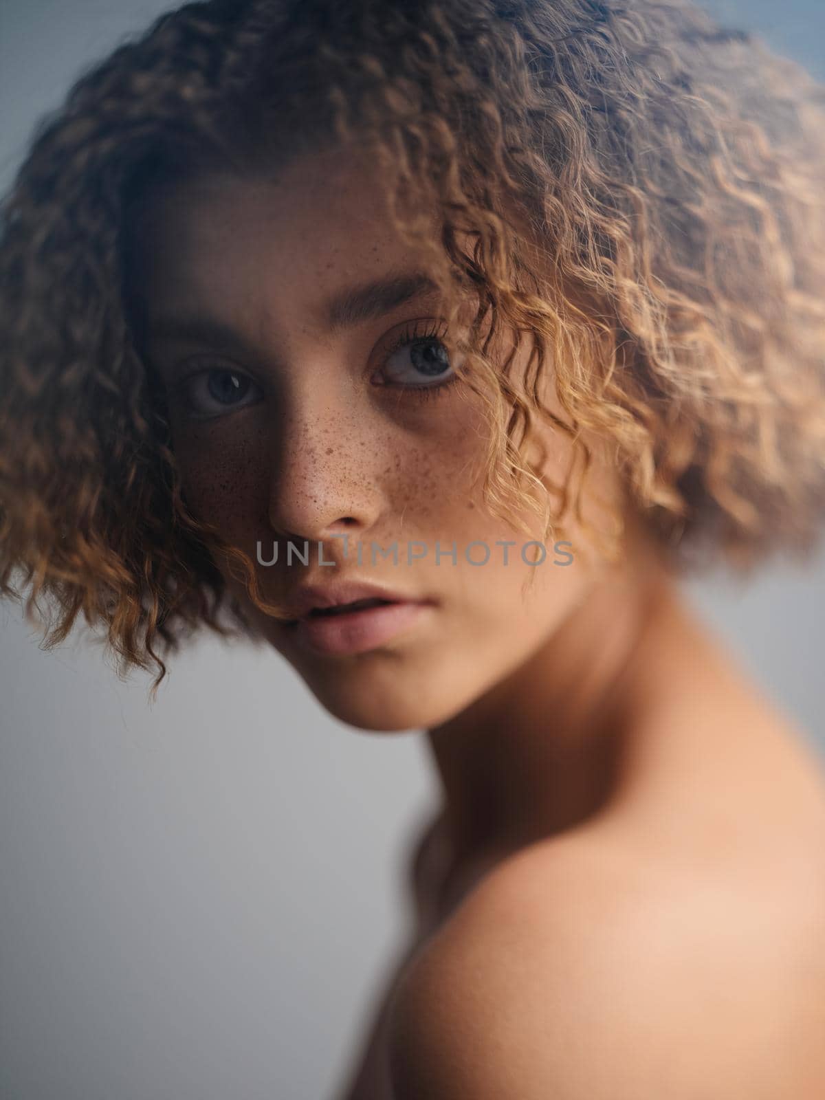 Portrait of a beautiful woman on a light background curly hair naked shoulders blue eyes. High quality photo