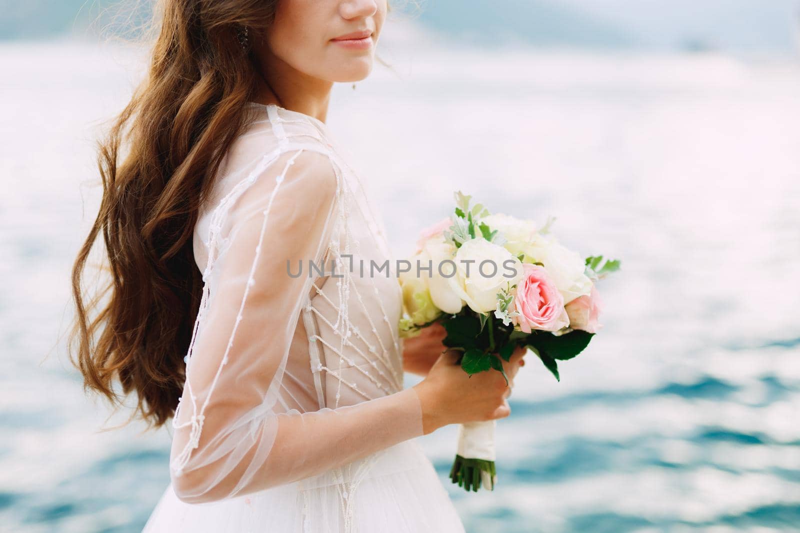 The bride holds a bouquet of roses in her hands and stands on the pier in the Bay of Kotor, close-up by Nadtochiy