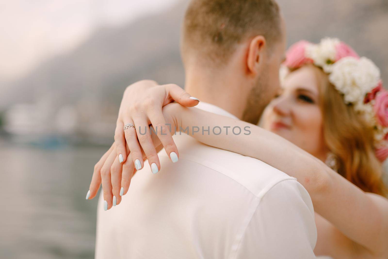 The bride and groom hug on the pier, the bride in a delicate wreath wrapped her arms around the groom's neck by Nadtochiy