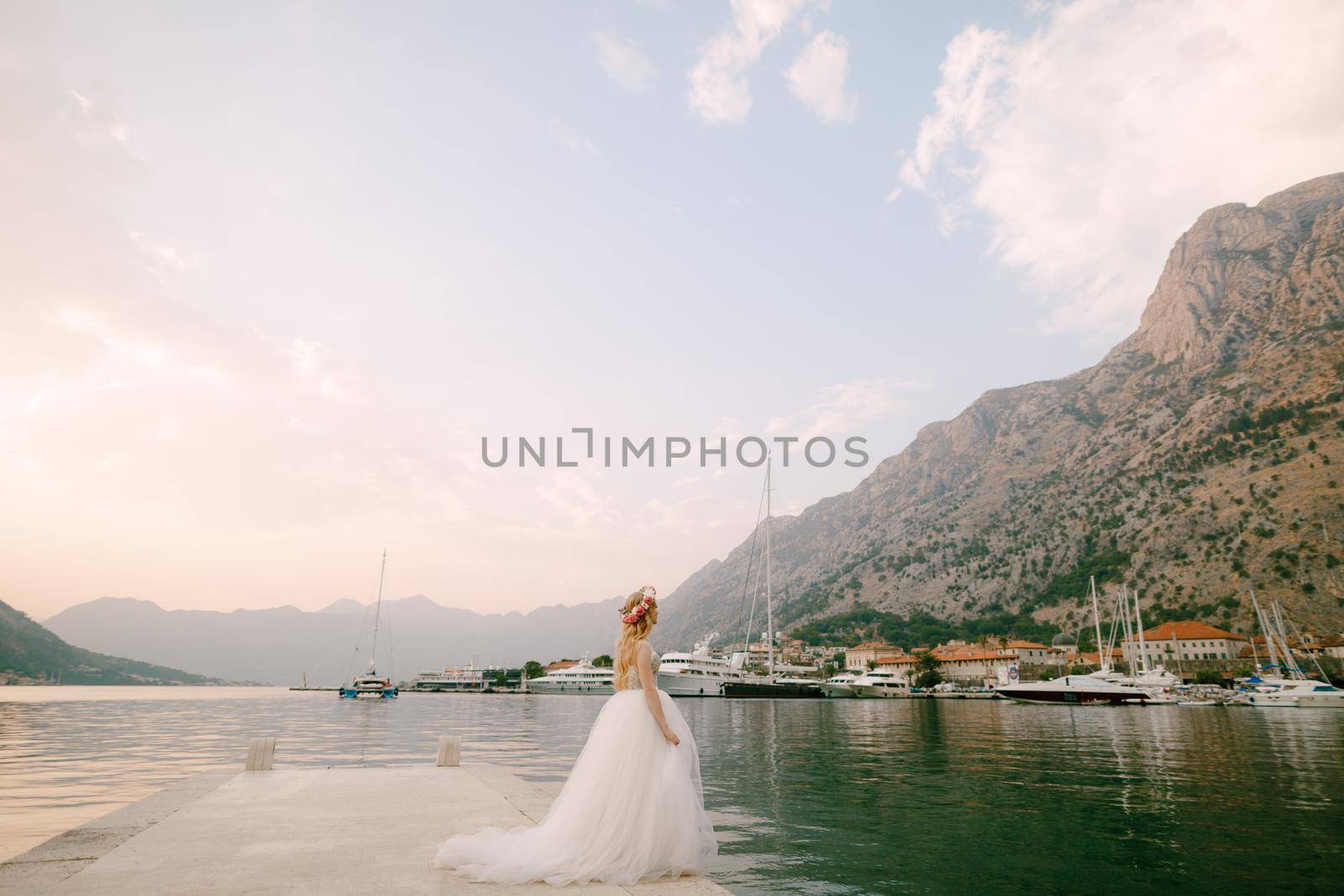 A bride in a delicate wreath of roses stands on a pier near Kotor in the Bay of Kotor. High quality photo